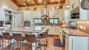 A kitchen with a large island, bar stools, white cabinets, a stainless steel range hood, and a wooden ceiling. - Lakefront Winnsboro Home w/ 20+ Acres! (Winnsboro)