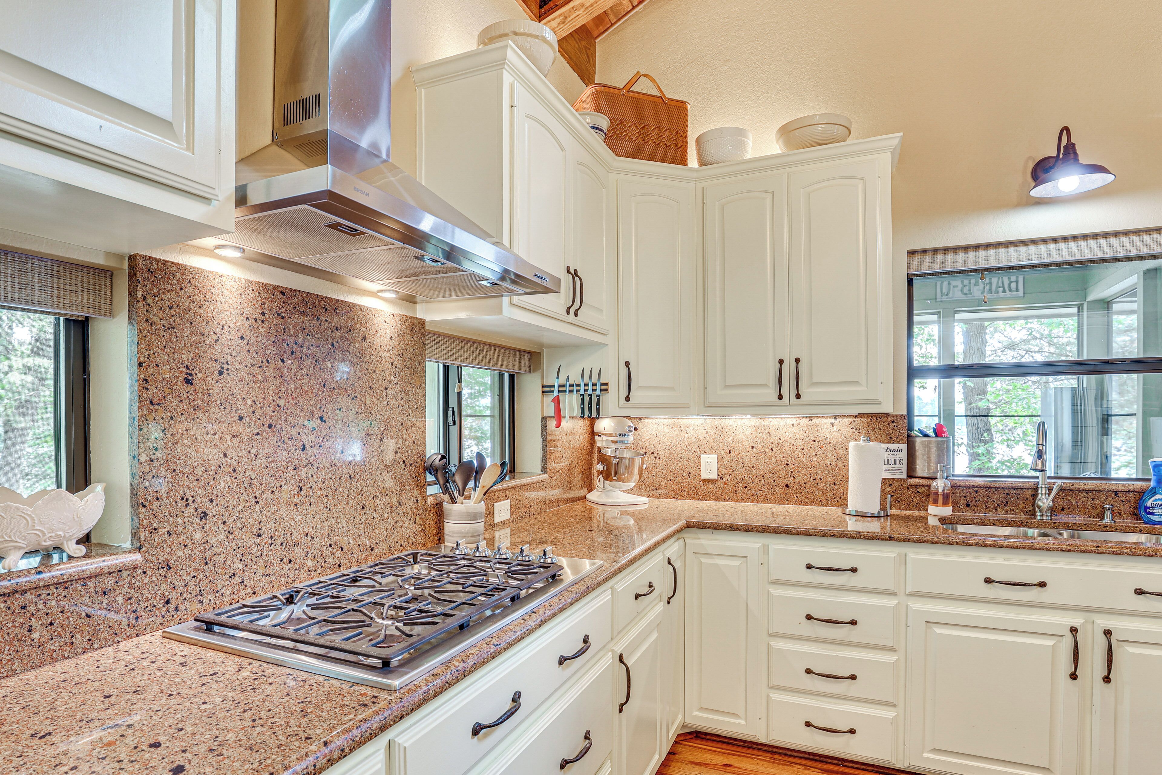 A kitchen with white cabinets, granite countertops, a gas stove, and a window with a view of trees.