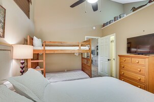 Un dormitorio con literas, un aparador, un televisor y una puerta que da a otra habitación.