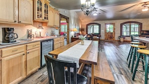 A spacious kitchen with wooden cabinets, a central island, and a dining area with a long wooden table and stools. - Walk to Lake Texoma: Family Home w/ Fire Pit! (Kingston)