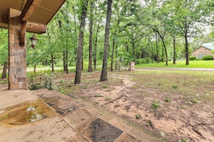 A covered patio area with stone columns, a lantern, and a lawn with trees.