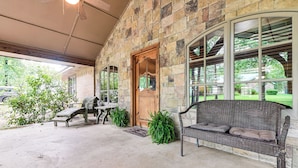 A covered patio with a stone wall, a wooden door, a wicker sofa, and a bench. - Walk to Lake Texoma: Family Home w/ Fire Pit! (Kingston)