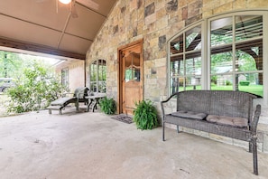 A covered patio with a stone wall, a wooden door, a wicker sofa, and a bench. - Walk to Lake Texoma: Family Home w/ Fire Pit! (Kingston)
