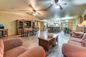 A spacious living room with a wooden floor, a ceiling fan, and a dining area with a bar. - Walk to Lake Texoma: Family Home w/ Fire Pit! (Kingston)