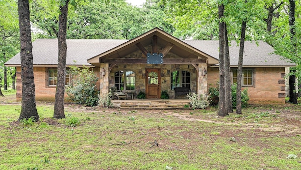 A rustic lodge with a stone facade, a prominent front porch, and a large wooden sign. - Walk to Lake Texoma: Family Home w/ Fire Pit! (Kingston)