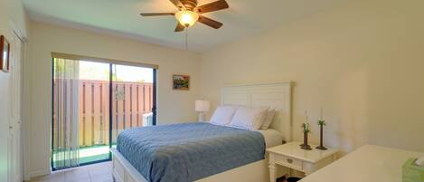 A bedroom with a bed, a nightstand, a ceiling fan, a window with blinds, and a door leading to a balcony.
