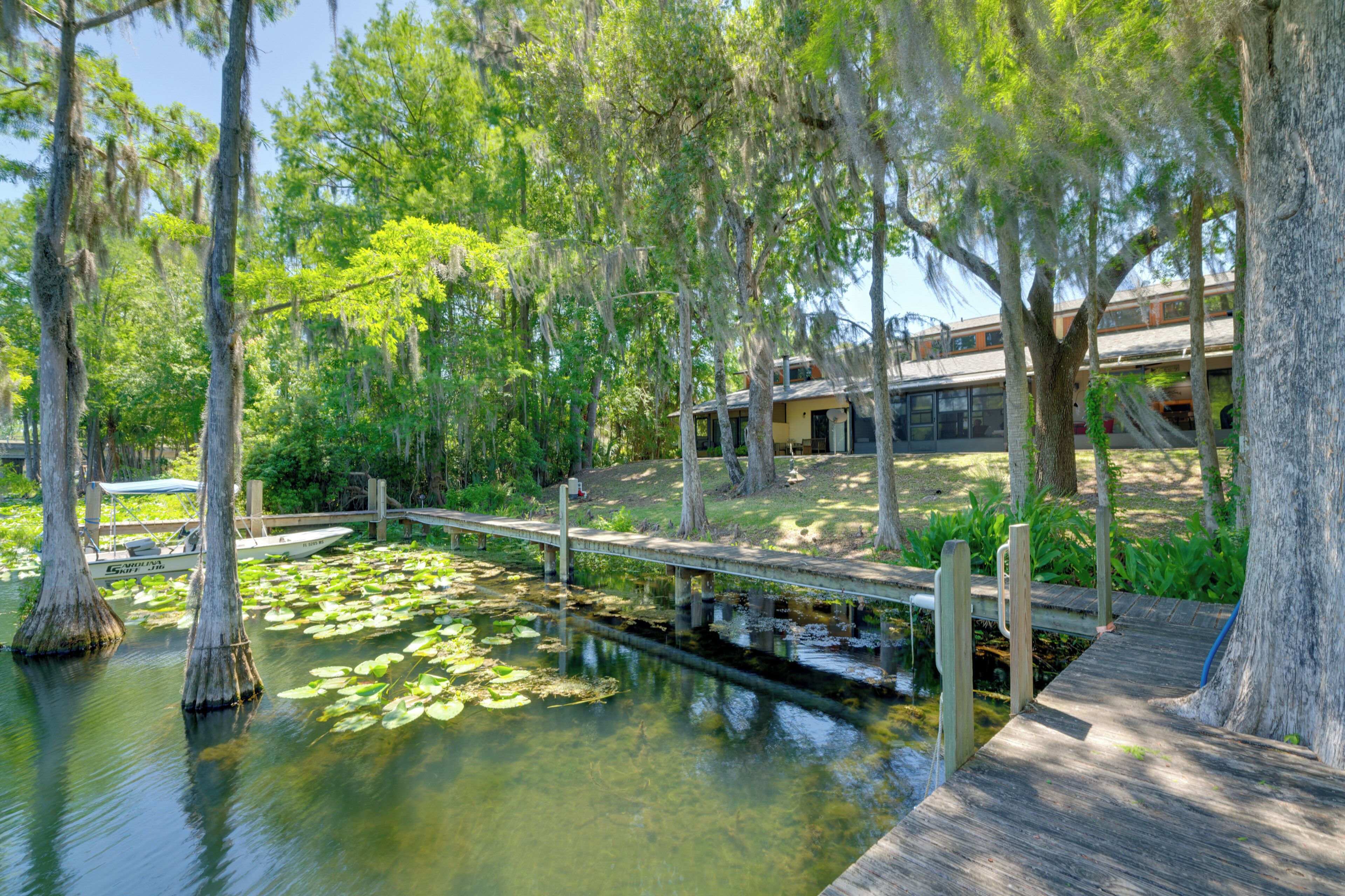 A serene waterway with a wooden bridge, surrounded by trees and a building in the background.