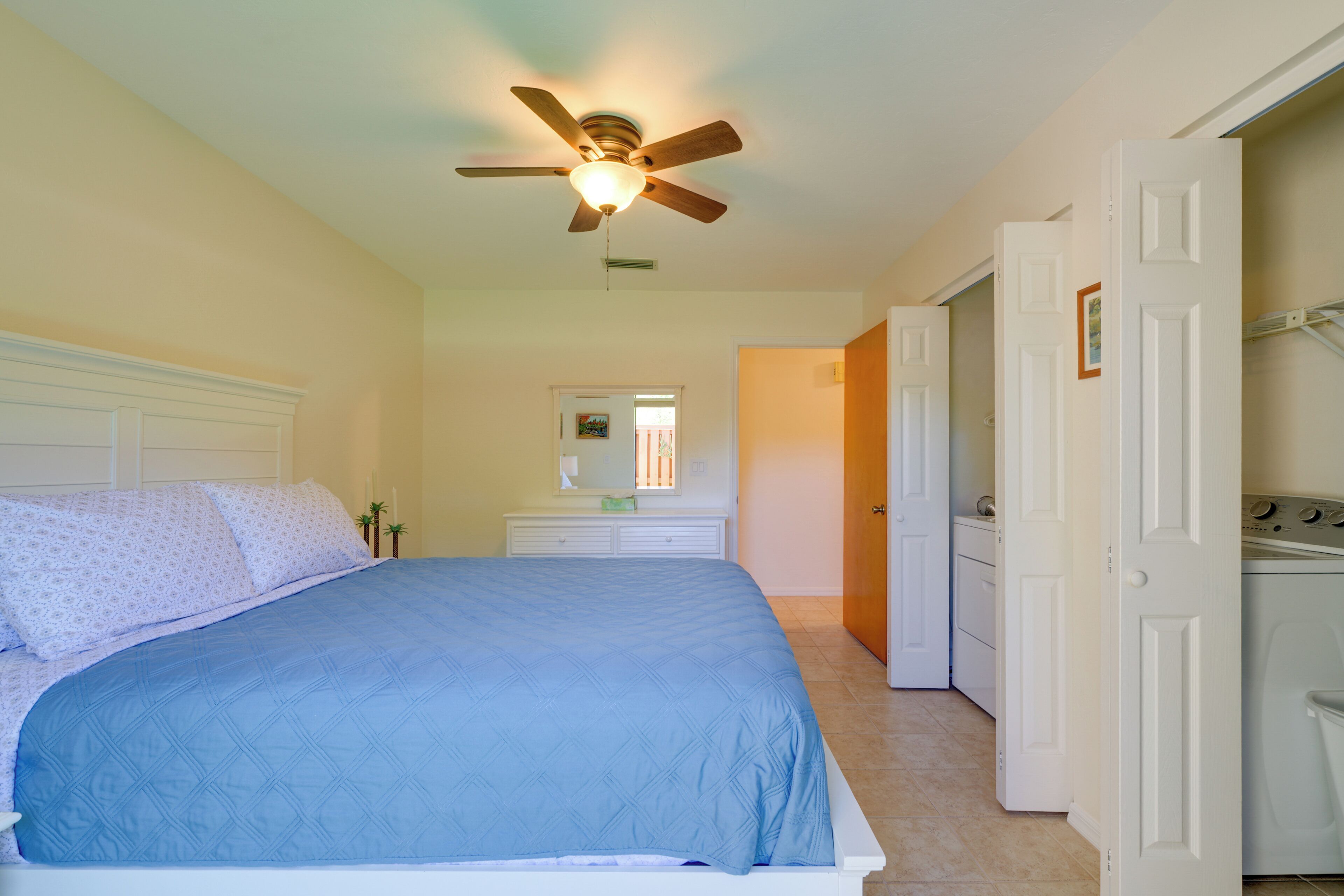 Un dormitorio con cama, ventilador de techo, cómoda y lavadora.