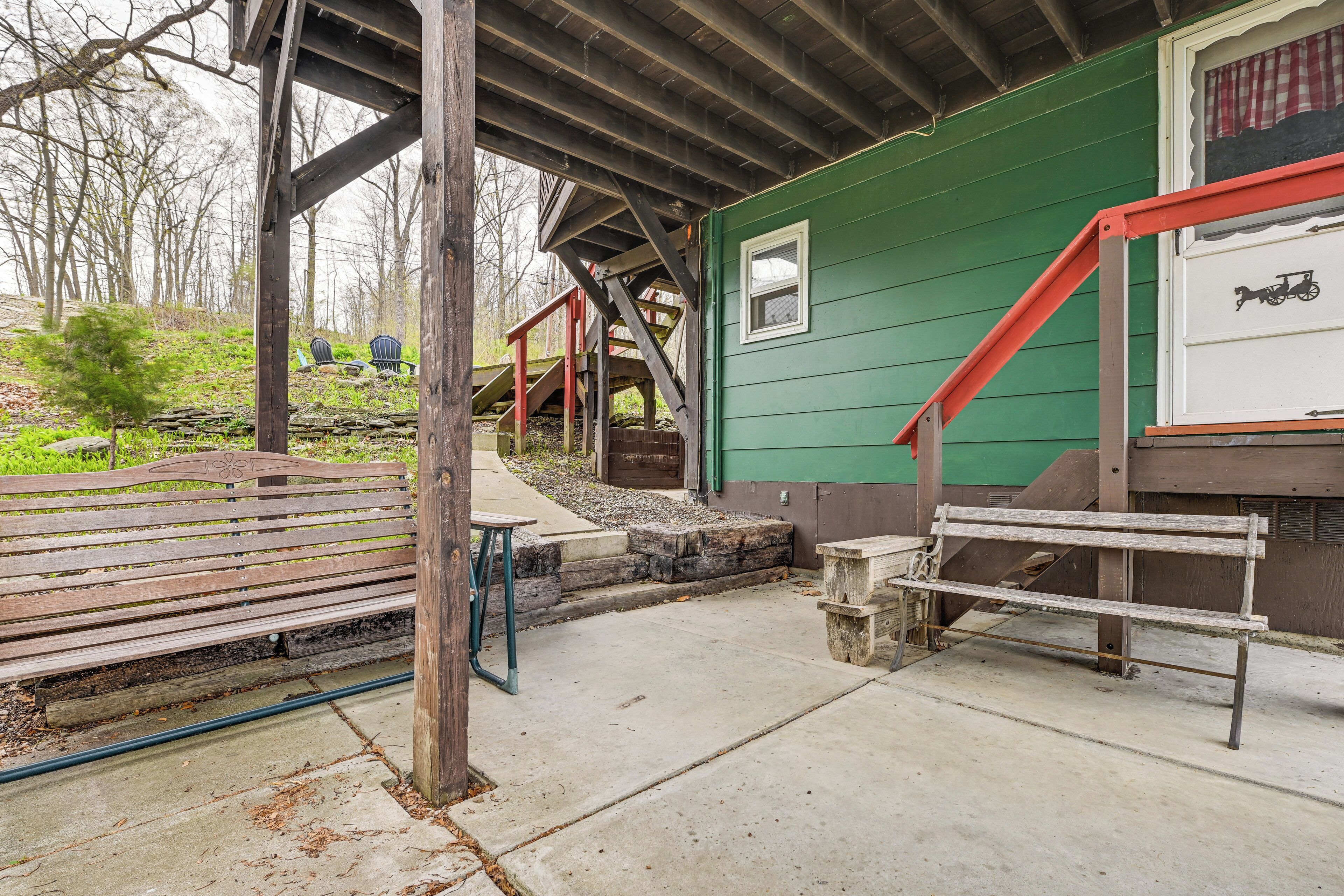 A wooden bench, a concrete pathway, a green building with a red staircase, and a small window with a toy car.