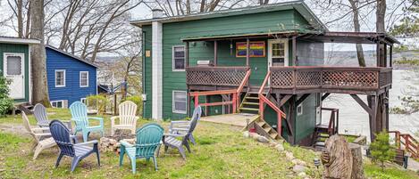A cabin with a deck, outdoor chairs, and a view of the lake.