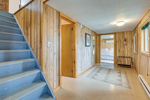 A wooden interior with a blue staircase, a door leading to another room, and a fire extinguisher on the wall. - Sunset Side of Seneca Lake! Family Home w/ Dock (Hector)