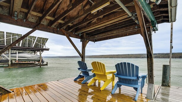 A wooden deck with three Adirondack chairs, a covered area, and a view of the water. - Sunset Side of Seneca Lake! Family Home w/ Dock (Hector)