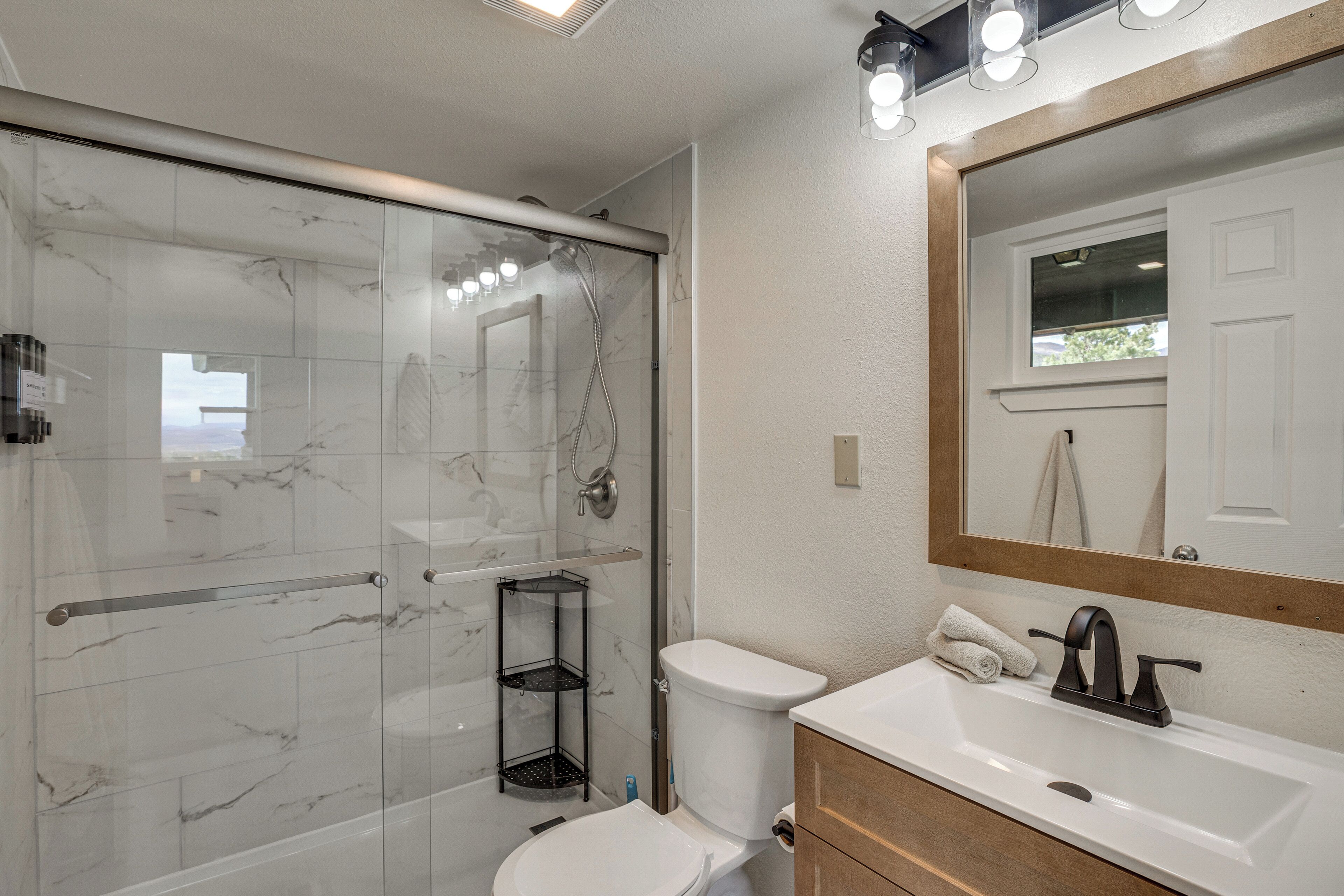A bathroom with a glass-enclosed shower, a white toilet, a sink with a mirror above it, and a towel rack.