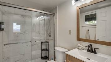 A bathroom with a glass-enclosed shower, a white toilet, a sink with a mirror above it, and a towel rack.