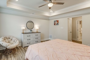 Une chambre à coucher comprenant un lit, une chaise, une commode, un ventilateur de plafond et une porte donnant sur une autre pièce.