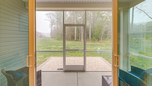 An open sliding glass door leading to a patio with a brick floor, wicker furniture, and a view of a grassy area with trees.