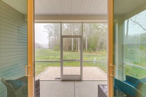 An open sliding glass door leading to a patio with a brick floor, wicker furniture, and a view of a grassy area with trees.