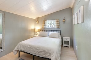 A bedroom with a bed, a nightstand, a window with curtains, and wall-mounted artwork.