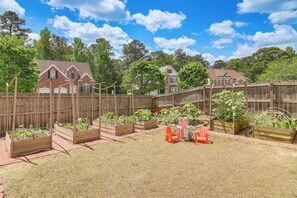 A backyard with raised garden beds, a wooden fence, and two houses in the background. - Families Welcome! Spacious Loganville Gem w/ Yard (Loganville)