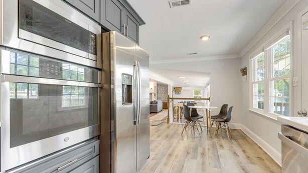A modern kitchen with stainless steel appliances, a dining area with a wooden table and chairs, and large windows. - Waterfront Lake Marion Home w/ Dock: Fish & Boat! (Manning)