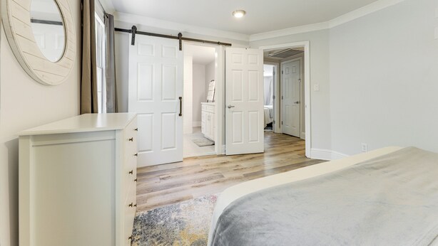 A bedroom with a bed, a dresser, and a door leading to another room.