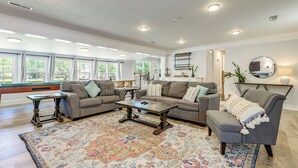 A spacious living room with a pool table, two sofas, a coffee table, and a large window.