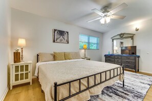 Un dormitorio con cama, mesita de noche, cómoda, ventilador de techo, ventana con persianas y un cuadro en la pared.