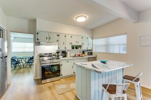A modern kitchen with white cabinets, a central island, and a dining area with chairs.