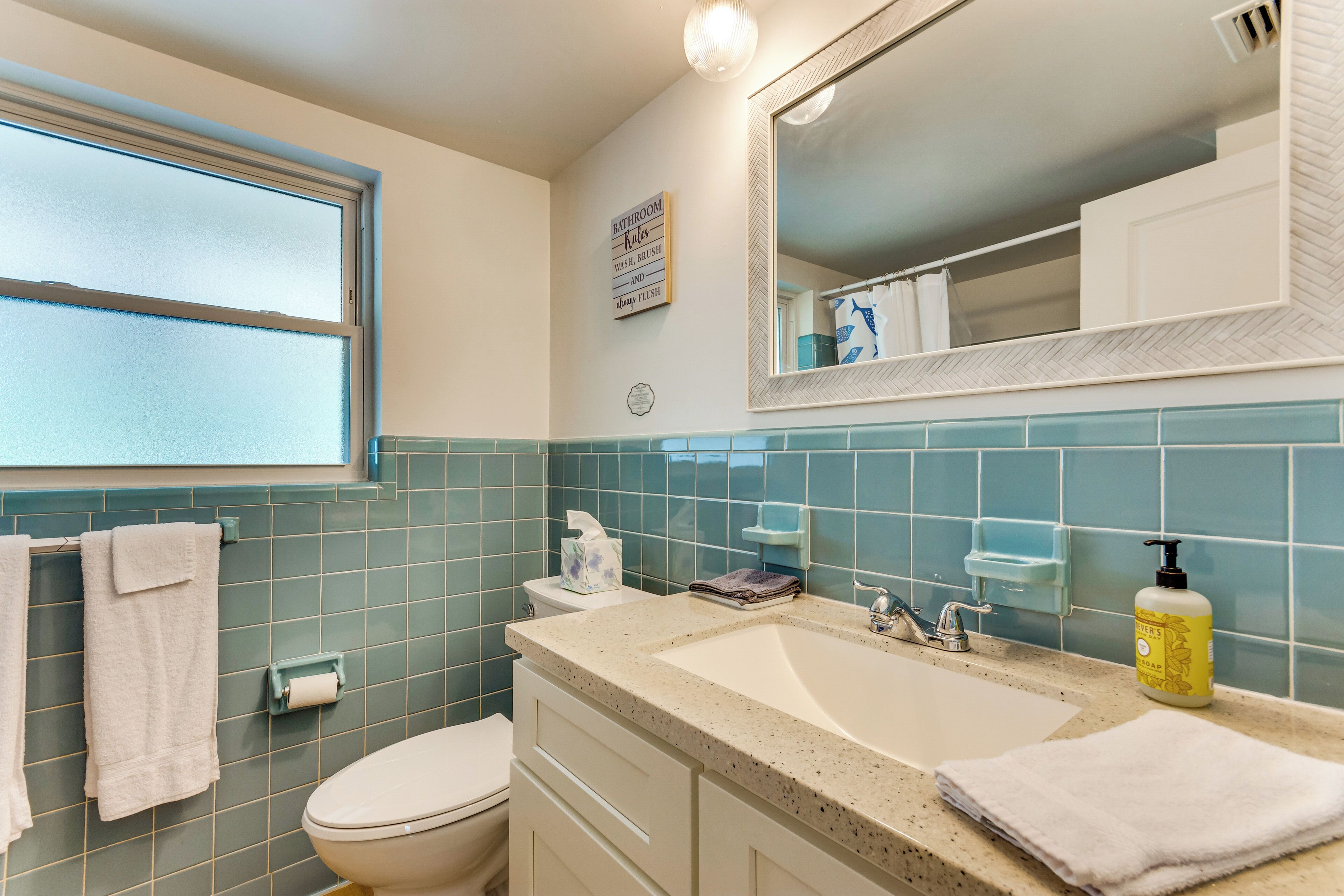 Ein Badezimmer mit Toilette, Waschbecken, Spiegel und blauen Fliesen.