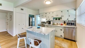 A modern kitchen with white cabinets, a marble island, stainless steel appliances, and a wooden floor.
