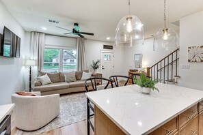 Una cocina moderna con una isla de mármol, luces colgantes, ventilador de techo y vistas al exterior.