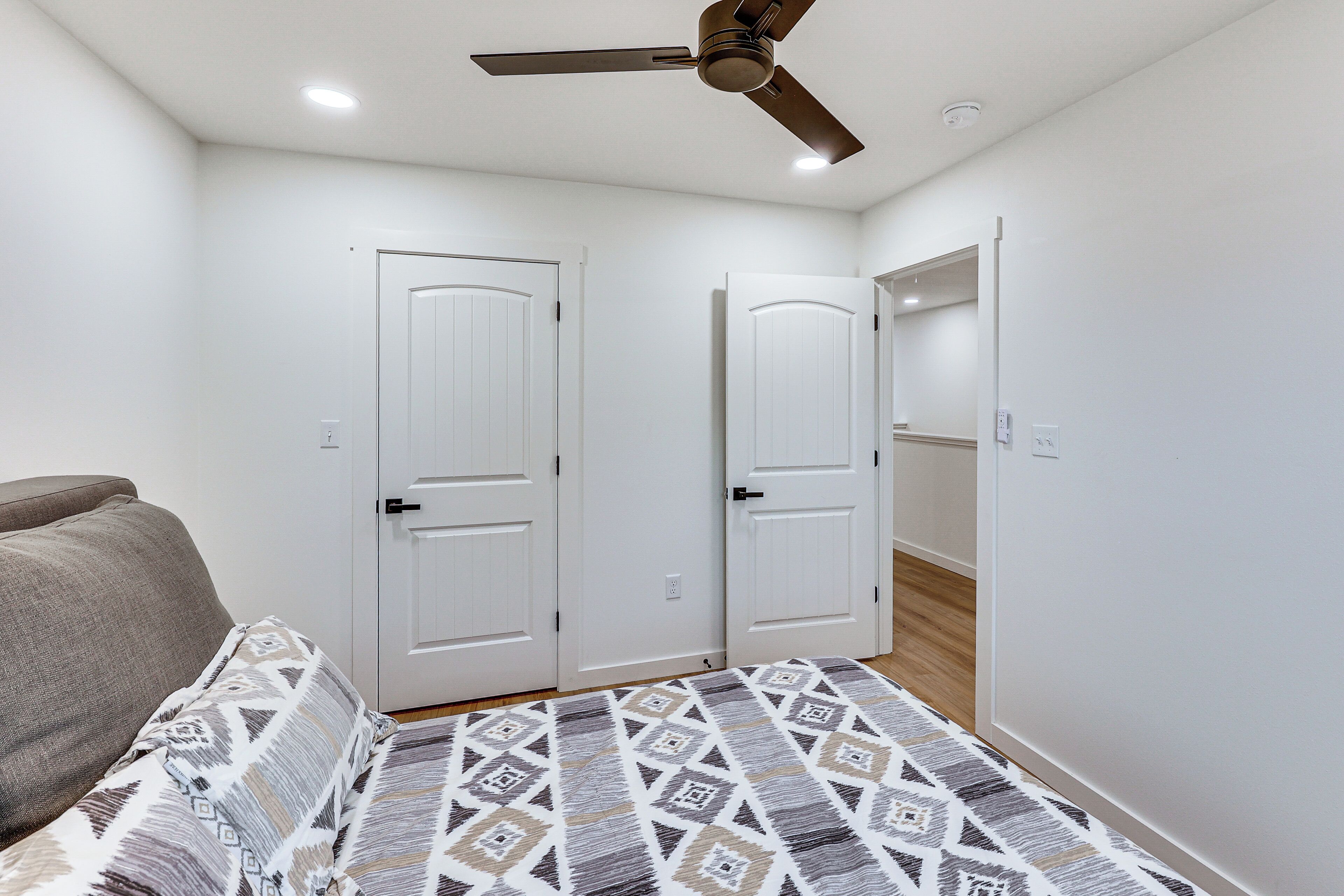 A bedroom with a bed, a ceiling fan, white doors, and a wooden floor.