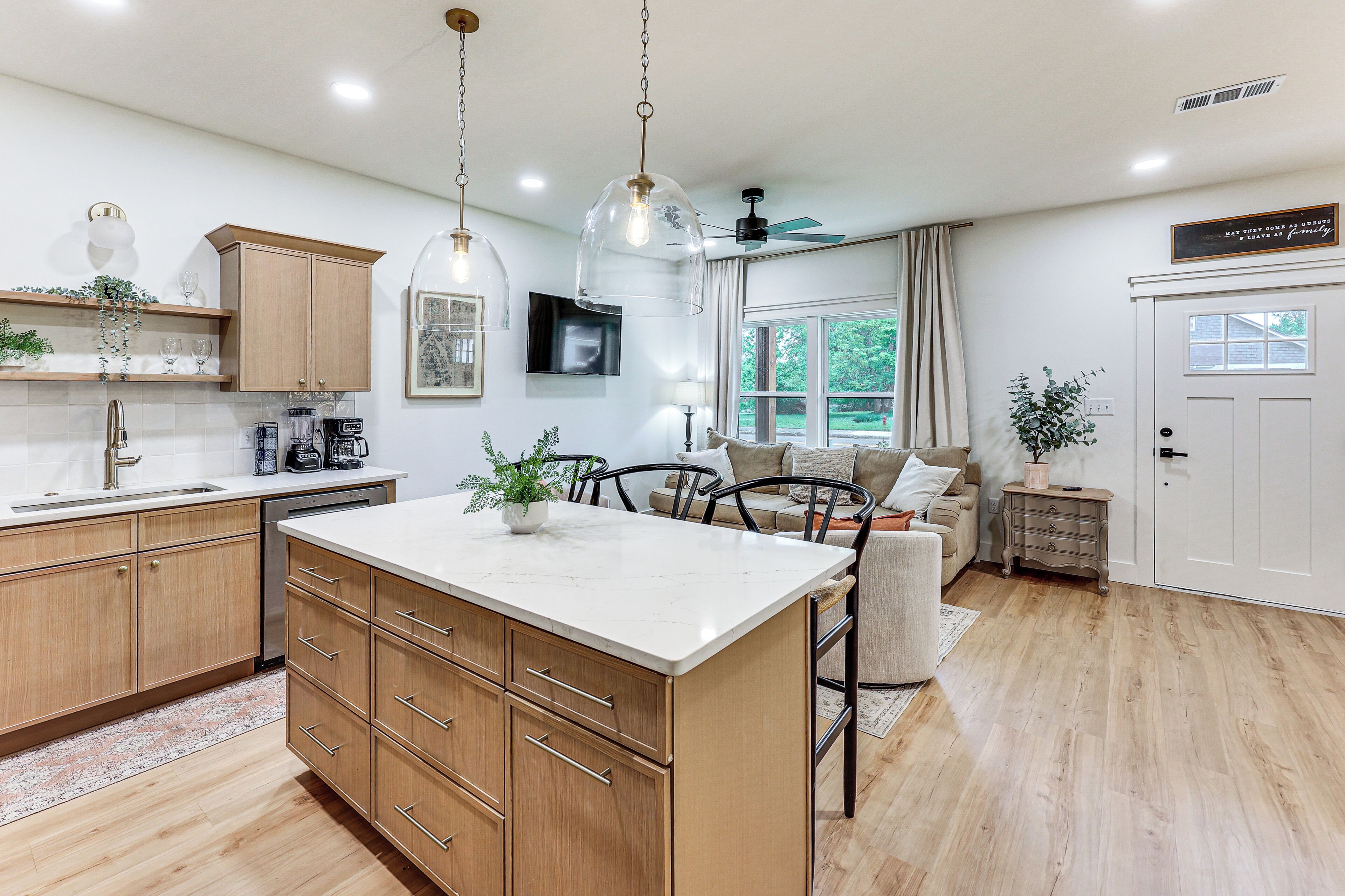 A modern kitchen with wooden cabinets, a marble countertop, and pendant lighting.