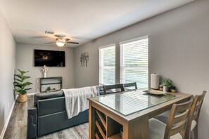 A dining area with a glass-top table, wooden chairs, a dark sofa, a ceiling fan, and a TV mounted on the wall. - Houston Hideaway w/ Rec Room, Putting Green & Hoop (Fresno)