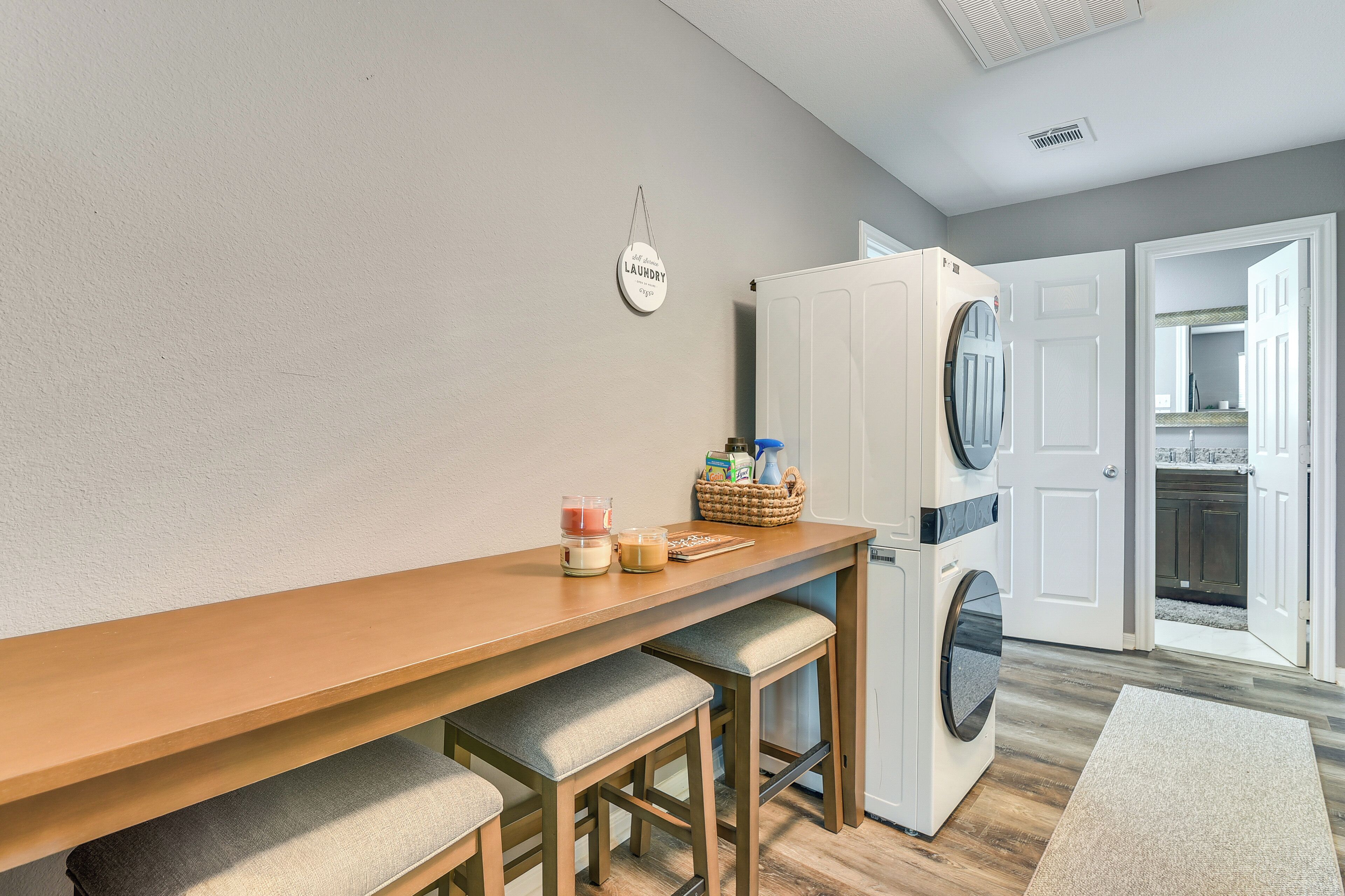A laundry room with a washing machine, a dryer, a wooden table with stools, and a basket with laundry supplies.