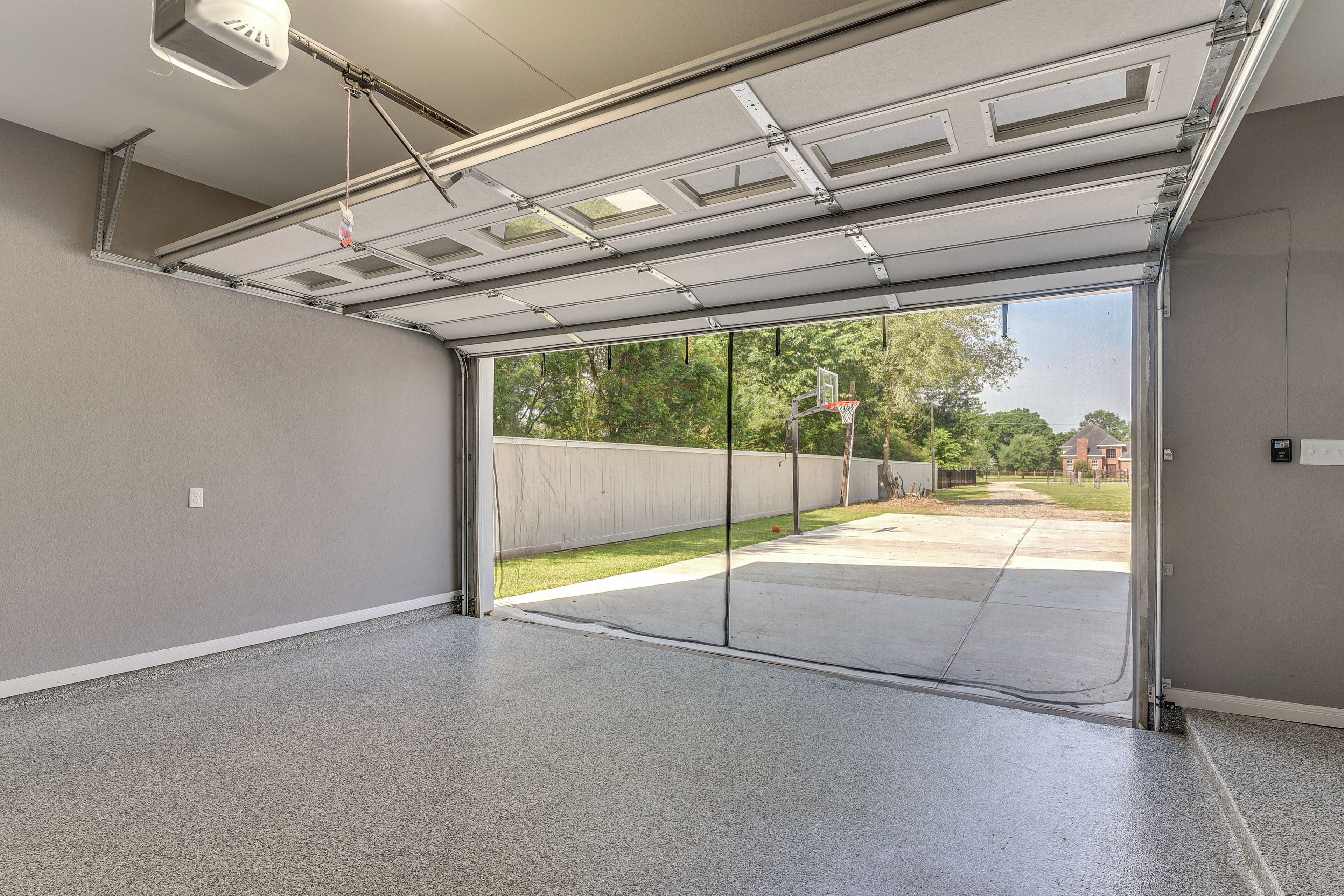 Eine Garage mit Rolltor, Betonboden und Blick auf eine Wohngegend mit Basketballkorb.