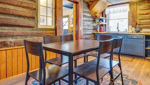 Een rustiek houten blokhut interieur met een eettafel, stoelen, een keukenhoek en een raam met jaloezieën.