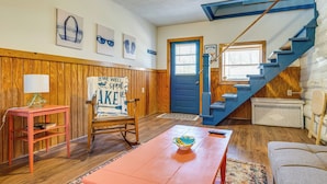 Een kamer met een houten vloer, een blauwe deur, een trap, een schommelstoel, een tafel en een bank.