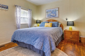 A bedroom with a bed, two bedside lamps, a nightstand, a welcome sign, and a painting on the wall.
