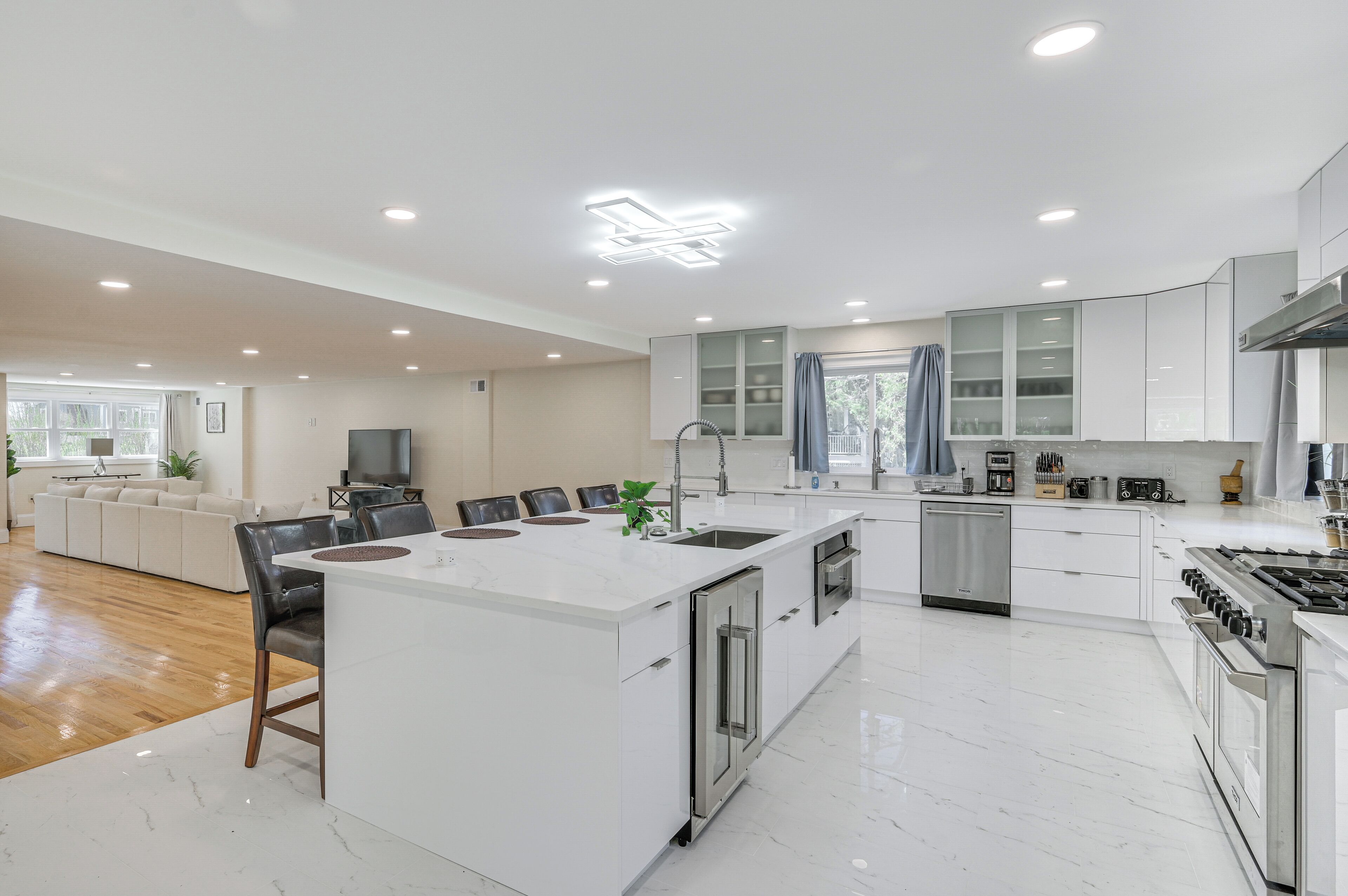 Cozinha moderna com ilha central, eletrodomésticos de aço inoxidável e área de refeições com sofá e cadeiras.