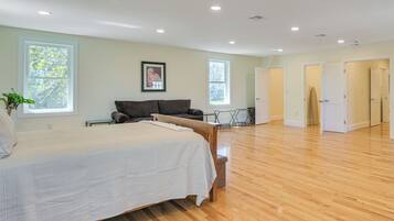 A spacious room with a large bed, a sofa, and a dining table. There are two windows and a door leading to another room.