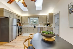 A modern kitchen with skylights, stainless steel appliances, and a dining table with a bowl of greens. - Hike, Work & Play! SLO Home: 2 Mi to Beaches (San Luis Obispo)