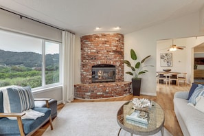 A living room with a brick fireplace, a sofa, a coffee table, and a view of the outdoors. - Hike, Work & Play! SLO Home: 2 Mi to Beaches (San Luis Obispo)