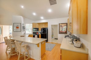 A modern kitchen with wooden cabinets, a central island with chairs, a refrigerator, and a microwave. - Game Room & On-site Golf Course! Lake Almanor Home (Westwood)