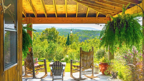 Une terrasse en bois, agrémentée de fauteuils à bascule et d’une table, qui offre une vue imprenable sur un paysage verdoyant.