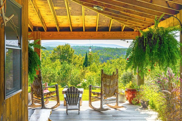 A wooden deck with rocking chairs and a table, overlooking a lush green landscape.