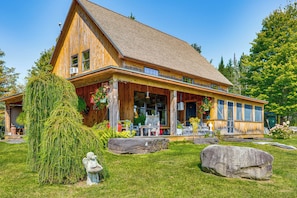 A wooden cabin with a large porch, a stone statue, and a large rock in the yard.