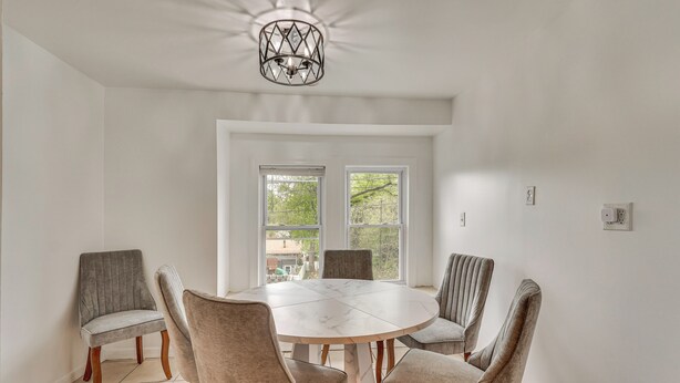 A dining area with a round table and six chairs, large windows, and a ceiling light fixture. - Nature & City Access! Family Home in North Jersey (Lincoln Park)