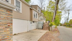 A residential area with a house featuring a brick exterior wall, a concrete driveway, and a street with a sidewalk. - Nature & City Access! Family Home in North Jersey (Lincoln Park)