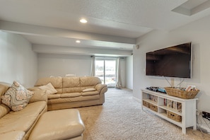 A living room with a beige sofa, a flat-screen TV mounted on the wall, and a bookshelf with books and a basket.